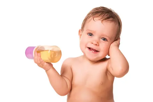 Bebê sorrindo segurando uma mamadeira com chá