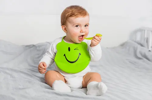 Bebê de babador comendo sozinho com uma colher