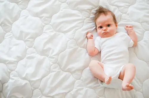 Bebê deitado de body branco com expressão contrariada