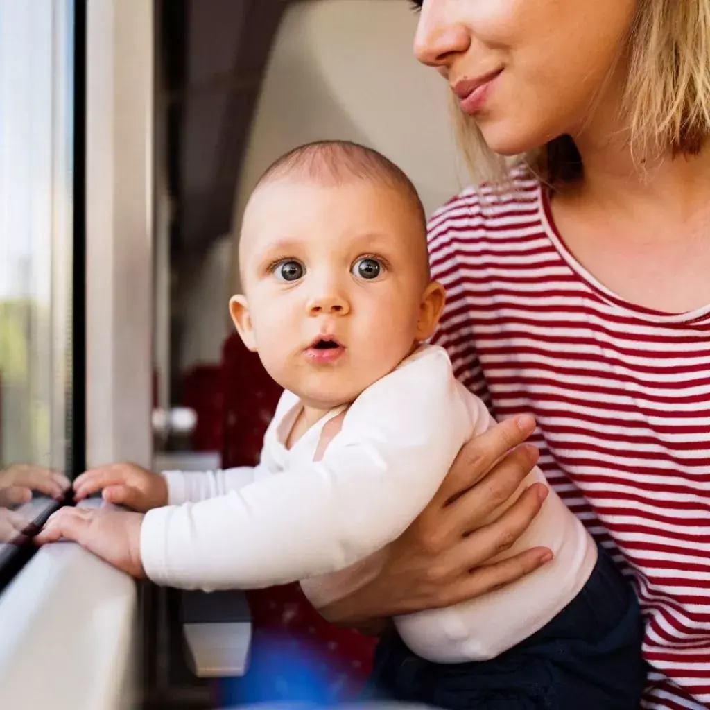 Mãe com o bebê no colo olhando pela janela de um trem