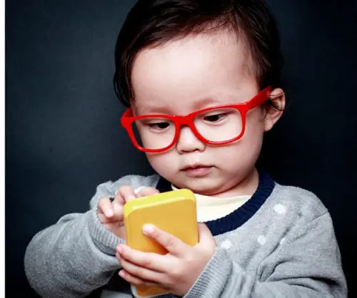 Criança pequena de óculos vermelhos distraída com um celular
